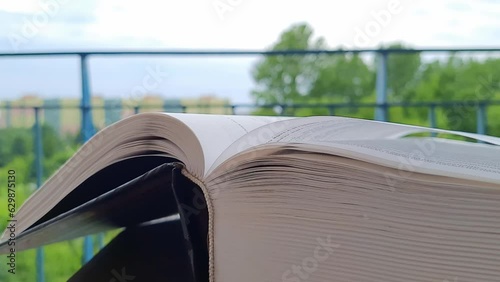 Wind is rustling the pages of the book. Open book outdoors. Book Lovers Day. Cozy weekend with a book. Modern and classical literature. Close-up.