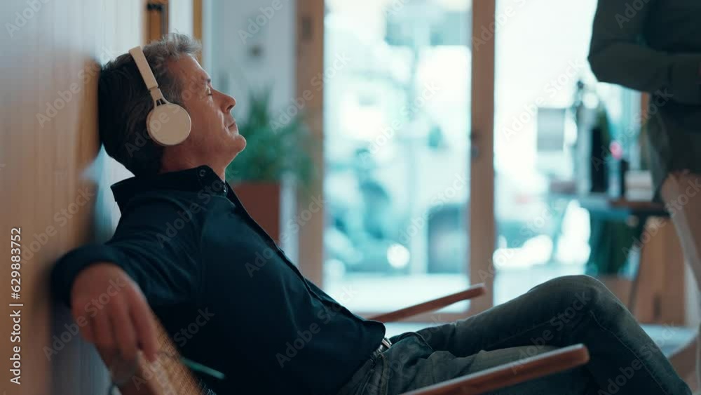 Video of mature handsome entrepreneur man relaxing while listening to music with headphones in a coworking place