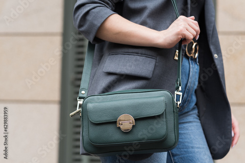 A woman holds a green handbag in the city. Close-up image. The concept of luxury