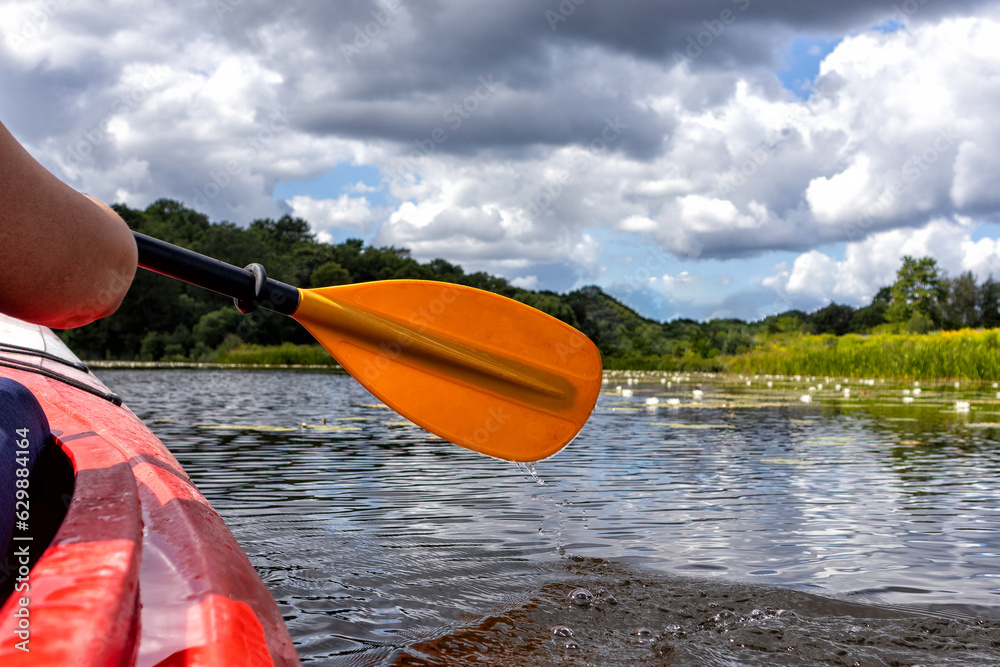 A man is paddling in a kayak on a lake with a cloudy sky in the background.
A man is paddling in a kayak on a lake with a cloudy sky in the background.
