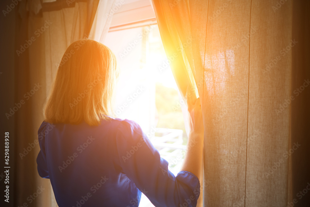 Fototapeta premium Woman opening curtains in the room at sunny morning.