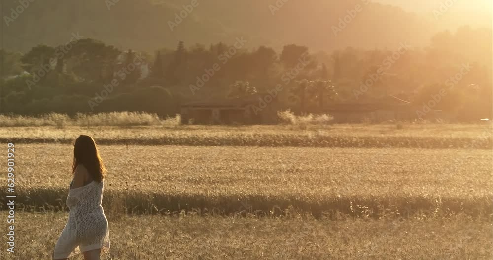 Chica andando por atardecer por el campo de trigo