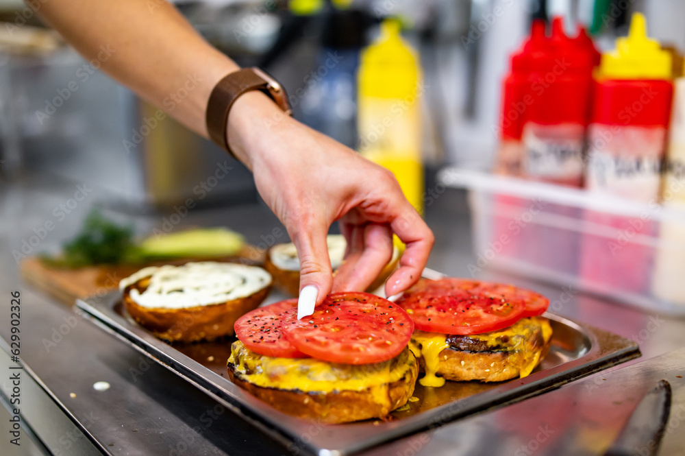 woman chef hand cooking burger with vegetables and meat on restaurant kitchen