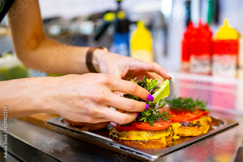 woman chef hand cooking burger with vegetables and meat on restaurant kitchen