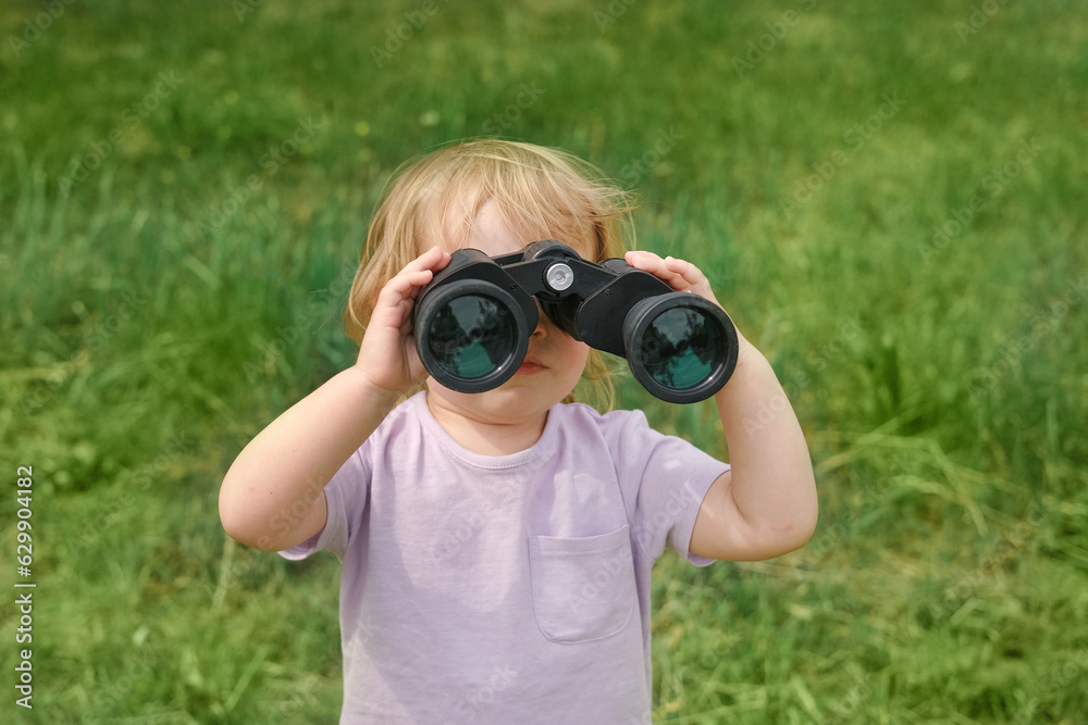 Little girl using binoculars in a forest. 2 years kid looking ahead. Smiling baby with spyglass. Adventure, Imagination, travel concept. Freedom, vacation. Happy child playing outdoor in summer field Little girl using binoculars in a forest. 2 years kid looking ahead. Smiling baby with spyglass. Adventure, Imagination, travel concept. Freedom, vacation. Happy child playing outdoor in summer field