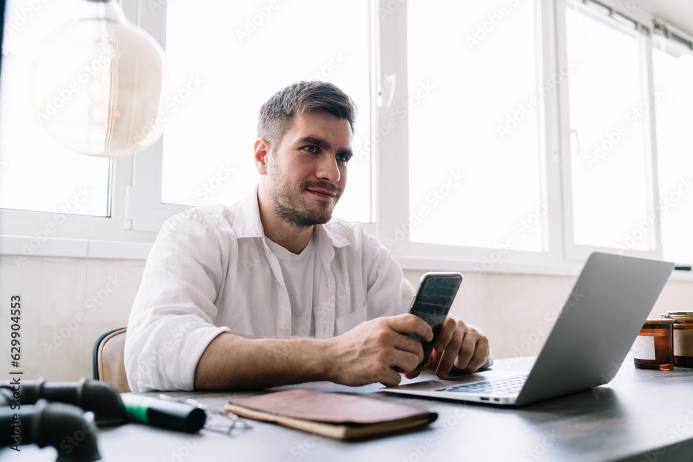 Smiling male entrepreneur using smartphone while working on computer
