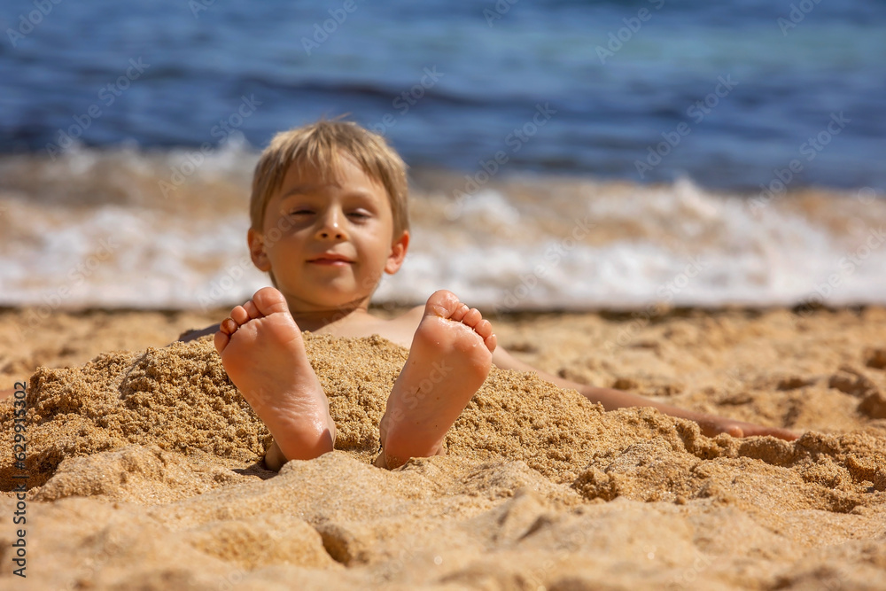 Child, tickling sibling on the beach on the feet with feather, kid cover in sand, smiling, laughing Child, tickling sibling on the beach on the feet with feather, kid cover in sand, smiling, laughing