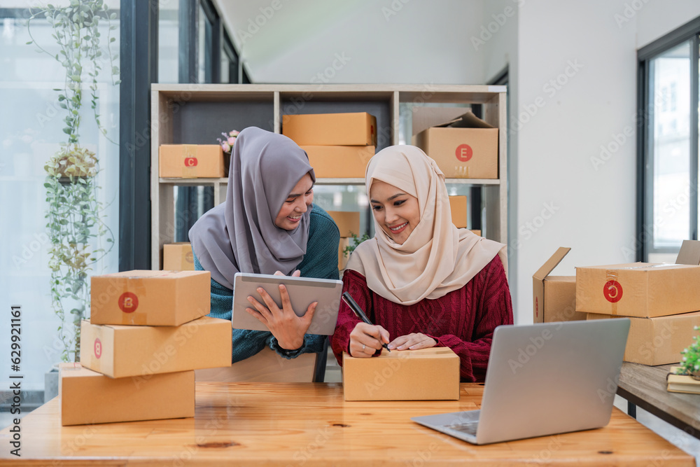 Muslim two woman freelancer sme business online shopping working on laptop computer and checklist order box at home Business online shipping and delivery concept Muslim two woman freelancer sme business online shopping working on laptop computer and checklist order box at home Business online shipping and delivery concept