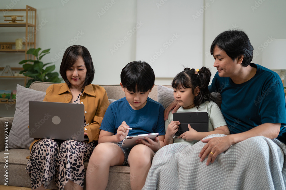 Happy parents with two kids using smartphone at home together, sitting on couch, smiling mother and father with little son and daughter looking at phone screen, having fun Happy parents with two kids using smartphone at home together, sitting on couch, smiling mother and father with little son and daughter looking at phone screen, having fun