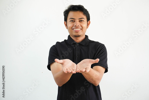 smiling young asian man posing on a white backdrop holding something with palms, offering to camera, wearing black polo t shirt.