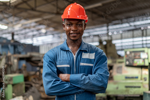 Portrait of smiling African American industrial worker man with helmet crossed arms in industry factory .happy confidence black male Engineer standing in manufacturing. good positive emotion job