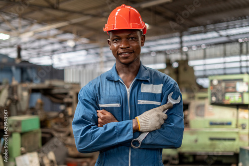 Portrait of smiling African American industrial worker man with helmet crossed arms holding wrench industry factory .happy confidence black male Engineer standing in manufacturing.