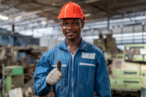Portrait of smiling African American industrial worker man with helmet show thumbs up in factory .happy confidence black male Engineer standing in manufacturing. good positive emotion job