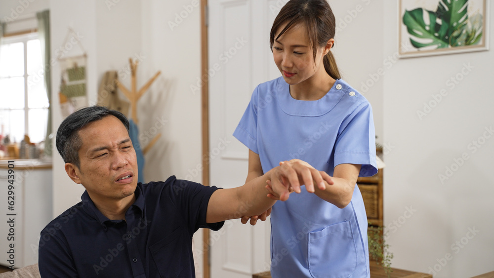 Obraz premium closeup of Asian mature Japanese male patient suffering pain while his personal care attendant is helping him do rehabilitation exercise by lifting his injured arm gently