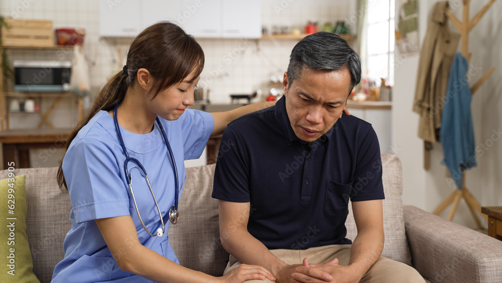 Fototapeta premium Asian female psychotherapist giving mental support to depressed elderly male patient. She taps his back gently while he is listening with head nodding at consultation