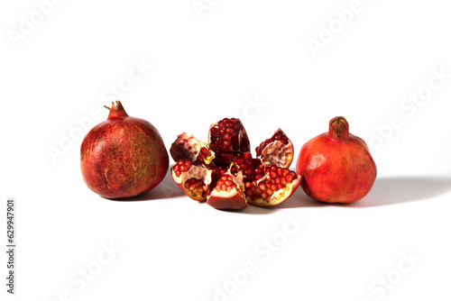 Three pomegranate fruits are depicted on a white background, one of which is broken into pieces.