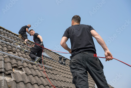 Workers passing power cable while installing solar panels on roof © Image Source