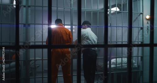 Warden brings guilty prisoner in jail cell and takes off handcuffs. African American man serves imprisonment term in correctional facility or detention center. Murderer in prison cell.