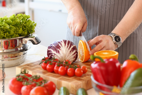 Closeup of chef hands cutting an orange on cutting board in kitchen. Healthy food and vitamin salad