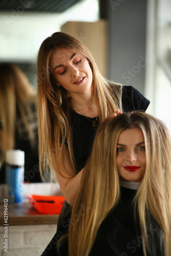 Smiling hairdresser doing hairstyle for young beautiful woman sitting in beauty salon. Hair care in beauty salon