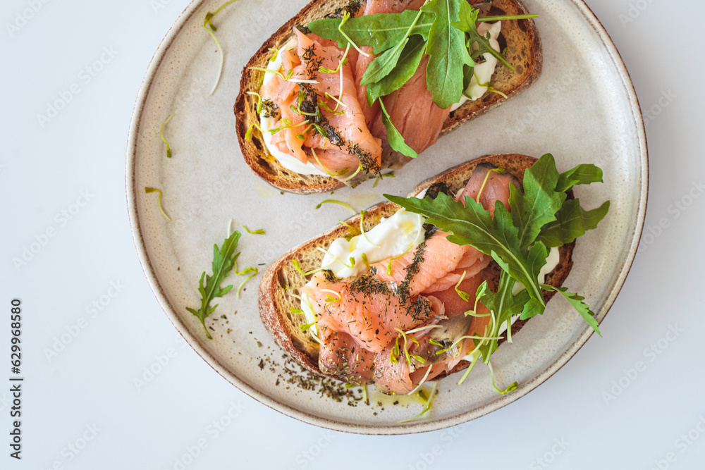 Breakfast toast with cream cheese, salmon, oil and arugula, white background. Keto diet recipe. Breakfast toast with cream cheese, salmon, oil and arugula, white background. Keto diet recipe.
