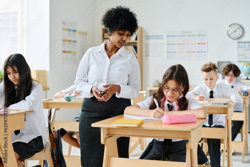 African American teacher having lesson with pupils at school while they sitting at desk and making notes in notebooks African American teacher having lesson with pupils at school while they sitting at desk and making notes in notebooks
