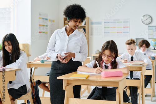 African American teacher having lesson with pupils at school while they sitting at desk and making notes in notebooks
