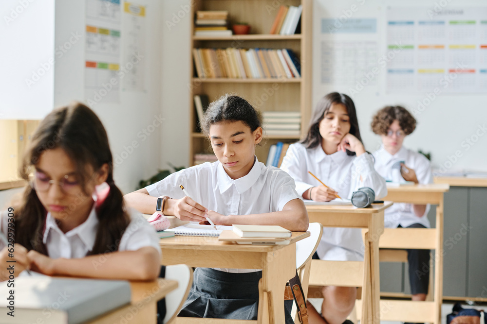 Group of school children sitting at desks and making notes in their notebooks during lesson at school