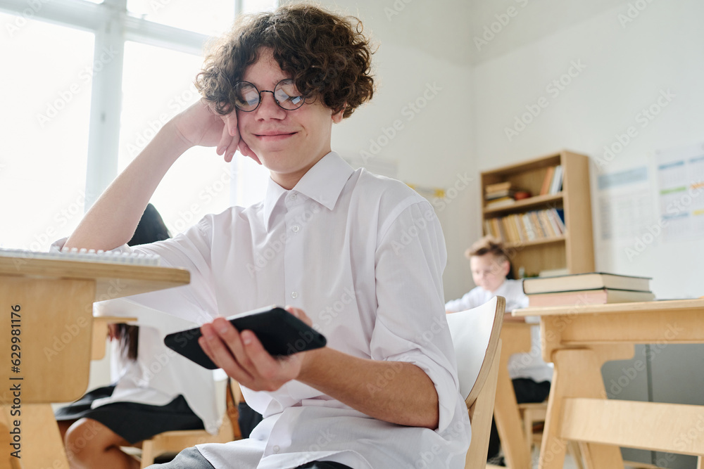 Student sitting at desk and using smartphone during lesson at school