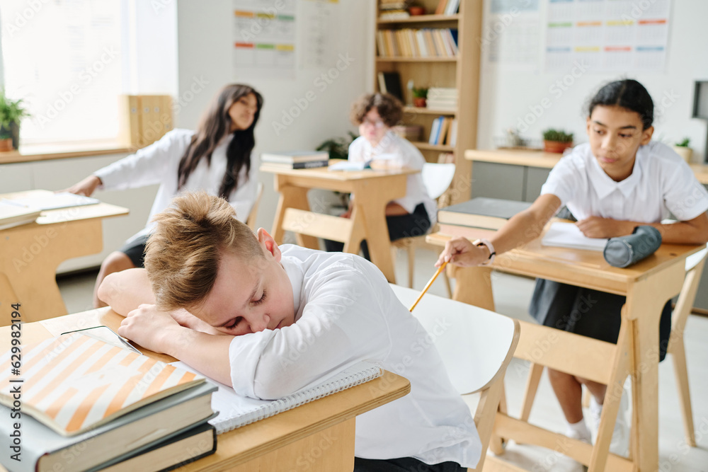 Obraz premium Schoolboy sleeping at desk at lesson while his classmate waking him up