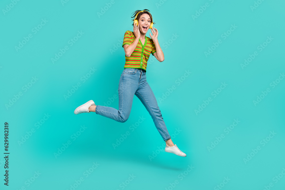Full length portrait of active pretty person hands touch headphones jumping isolated on turquoise color background Full length portrait of active pretty person hands touch headphones jumping isolated on turquoise color background