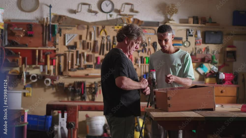 Candid scene of senior carpenter and junior apprentice young man working at carpentry workshop