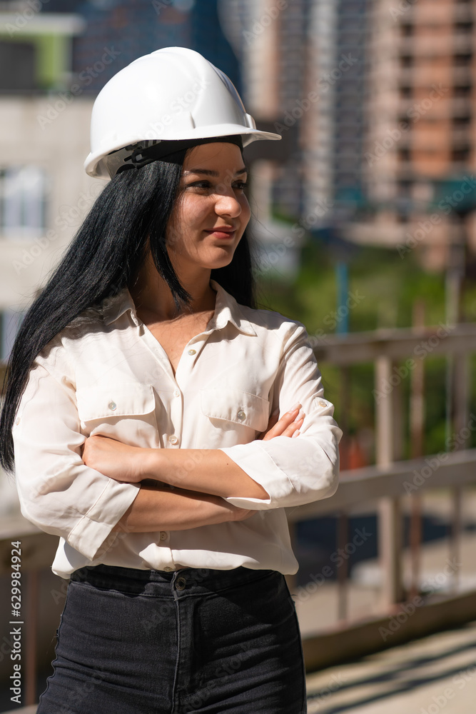 Young beautiful female engineer in a hard hat at a construction site on a sunny day looks away, copy space. Vertical photo Young beautiful female engineer in a hard hat at a construction site on a sunny day looks away, copy space. Vertical photo