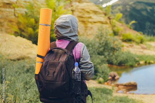 Girl tourist on a hike with a backpack and karemat. Back view.