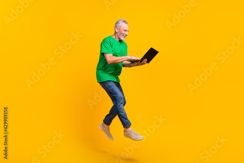 Full length profile portrait of excited carefree man jumping hold use netbook coworking isolated on yellow color background