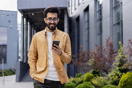 Wallpaper Mural Young successful businessman walking in the city outside office building, hispanic smiling happy with achievement results, holding phone, using online application outdoors. Torontodigital.ca