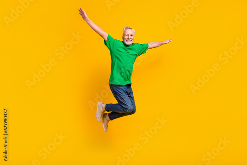 Full size portrait of active cheerful aged person jumping raise arms wings flying isolated on yellow color background © deagreez