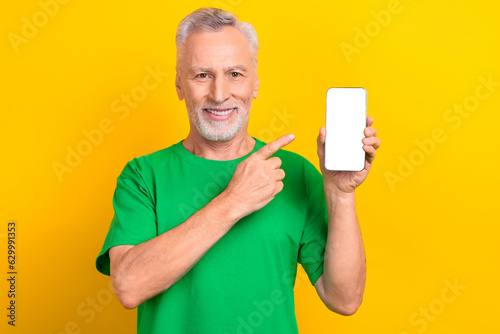 Photo of handsome aged man indicate finger hand hold empty space smart phone display isolated on yellow color background