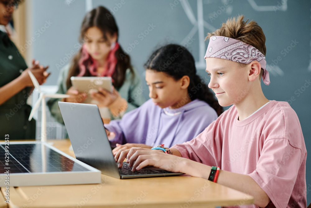 Schoolboy sitting at table in the classroom and working online on laptop Schoolboy sitting at table in the classroom and working online on laptop