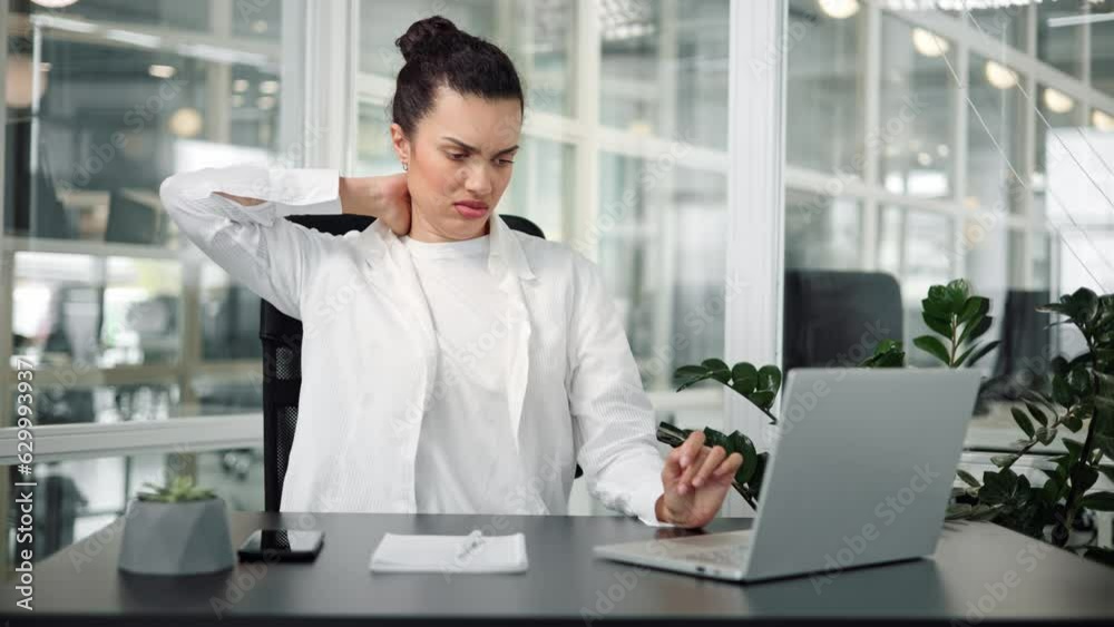 Tired young latin hispanic business woman massaging her neck and taking a break from working on laptop at the office company. Sad overworked female employee in massages and rubs sore muscles. Tired young latin hispanic business woman massaging her neck and taking a break from working on laptop at the office company. Sad overworked female employee in massages and rubs sore muscles.