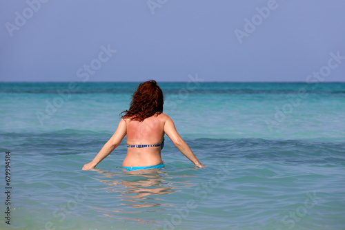Woman in bikini going to swim in blue sea water. Beach vacation in summer
