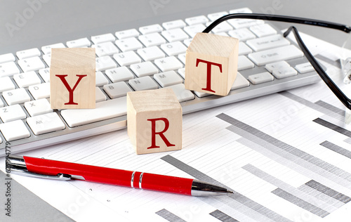 YRT written on a wooden cube on the keyboard with chart on grey background photo