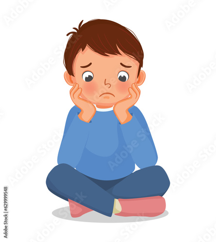 Sad little boy sitting on the floor with his chin resting on his hands