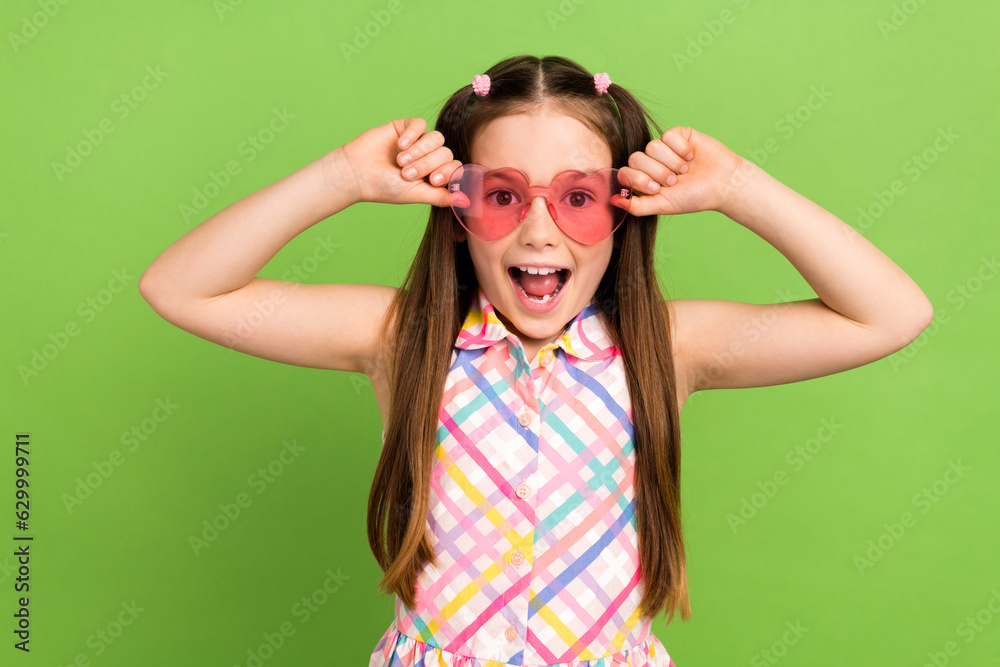 Photo of impressed positive girl hands touch heart shape sunglass open mouth isolated on green color background