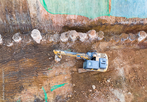 Excavator on earthmoving at construction site, aerial view.