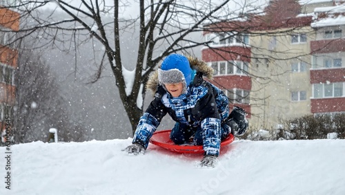 Joyful boy gliding down a snowy hill on plastic sleds, captured in slow motion for added emphasis on the fun and excitement of the experience.