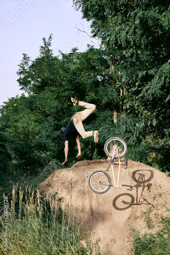 Dangerous sport. Young man riding on hill in park, forest on bmx bike, doing tricks and falling down. Concept of active lifestyle, sport, extreme, dynamics, hobby, freestyle