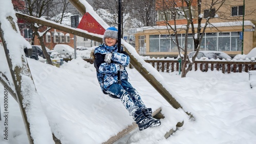 Cheerful smiling boy riding on the zipline at winter in public park. Children playing and having fun outdoors during winter holidays and weekend photo