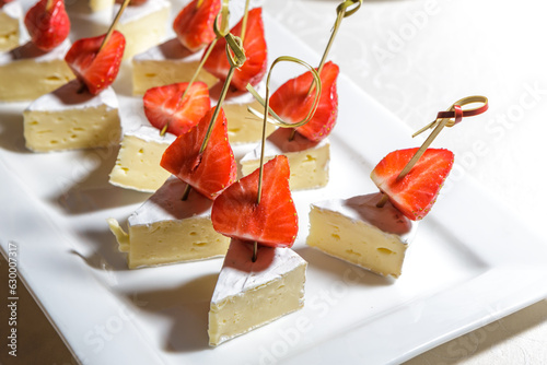 Canapes of ripe strawberries and cheese are on a tray.