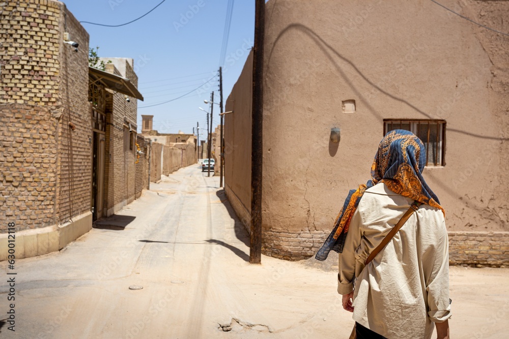 Woman walking through a city street, surrounded by quaint brick buildings in Yazd, Iran
